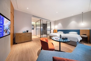 Habitació d'hotel moderna amb un llit, una taula de treball, una cadira i un televisor penjat a la paret.