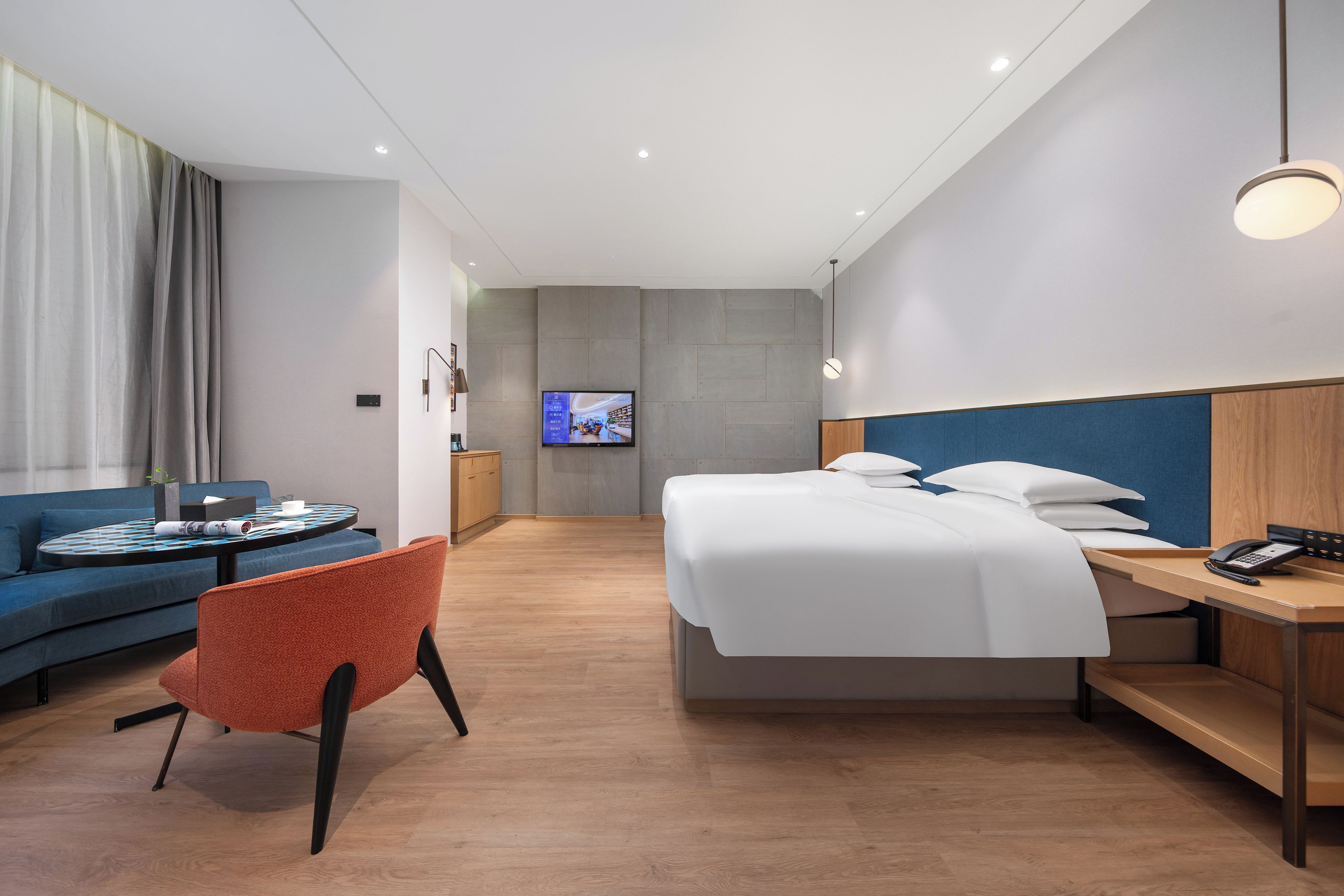 A hotel room with a bed, a desk with a phone, a sofa, a chair, and a TV on the wall.
