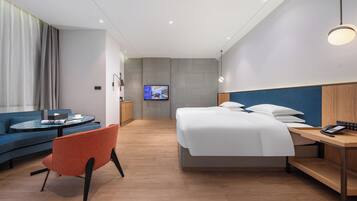 A hotel room with a bed, a desk with a phone, a sofa, a chair, and a TV on the wall.