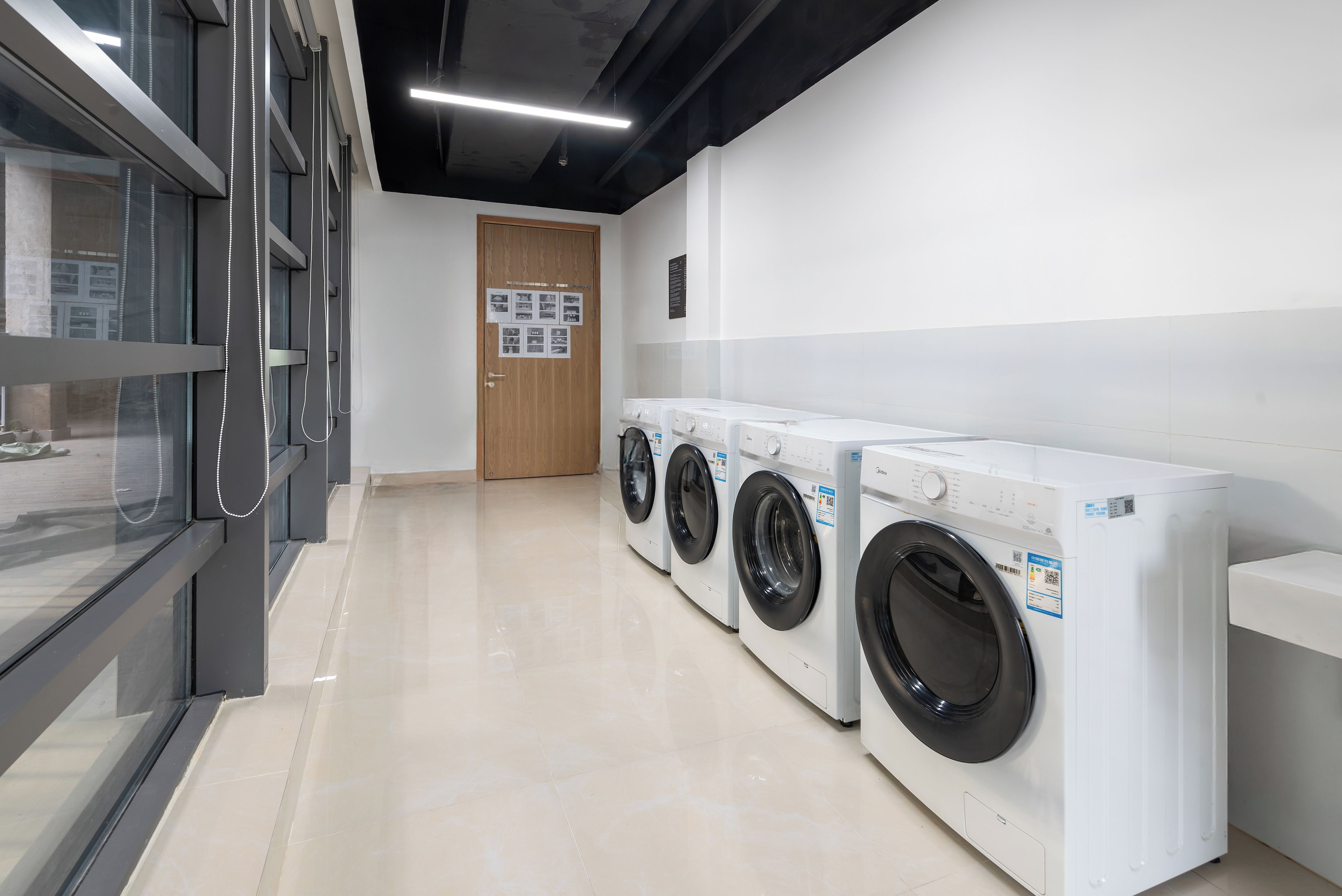 A laundry facility with multiple washing machines, a wooden door, and a tiled floor.
