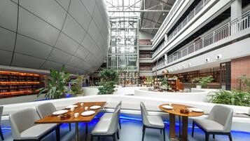 A spacious atrium with multiple levels, a central seating area with tables and chairs, and surrounding bookshelves.