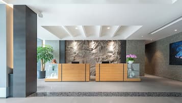 Zona de recepción con diseño moderno, que incluye un mostrador de recepción, una pared con textura similar a la piedra y una planta en maceta.
