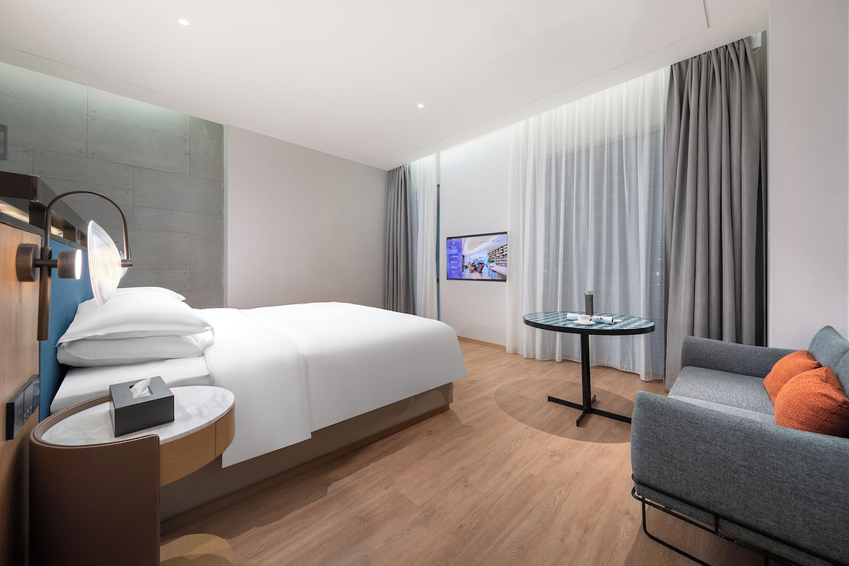 Habitació d'hotel moderna amb llit, escriptori, cadira, televisió i sofà.