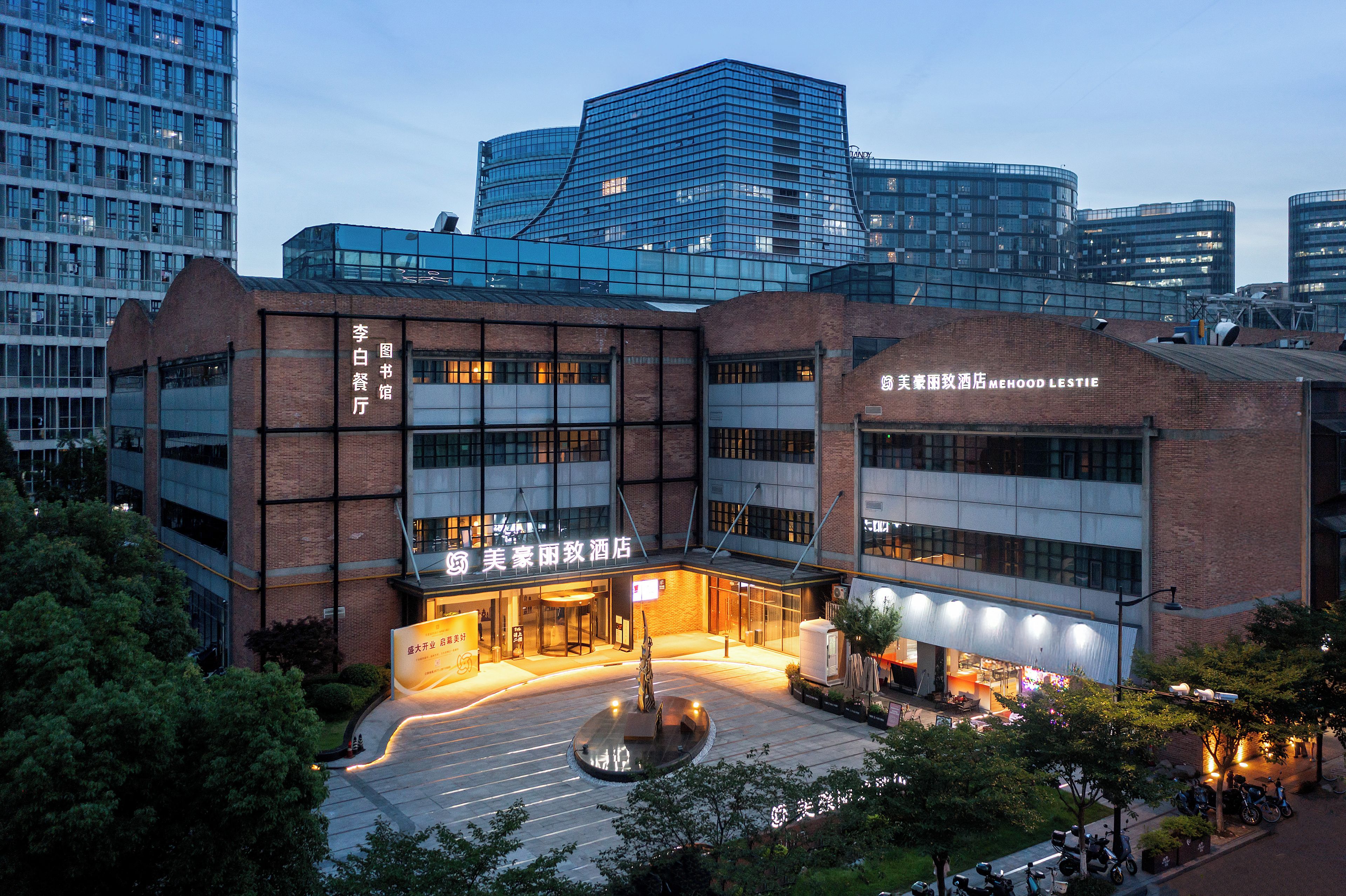 A hotel with a modern glass facade, a brick lower section, and a well-lit entrance.