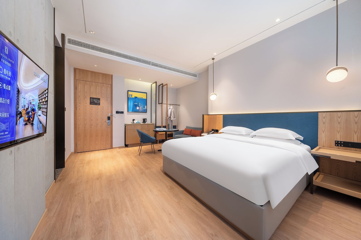 Habitació d'hotel moderna amb un llit gran, una taula de treball, una cadira, un televisor i un armari.