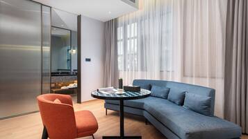 Una habitación de hotel moderna con un sofá gris, una mesa redonda y una silla roja.