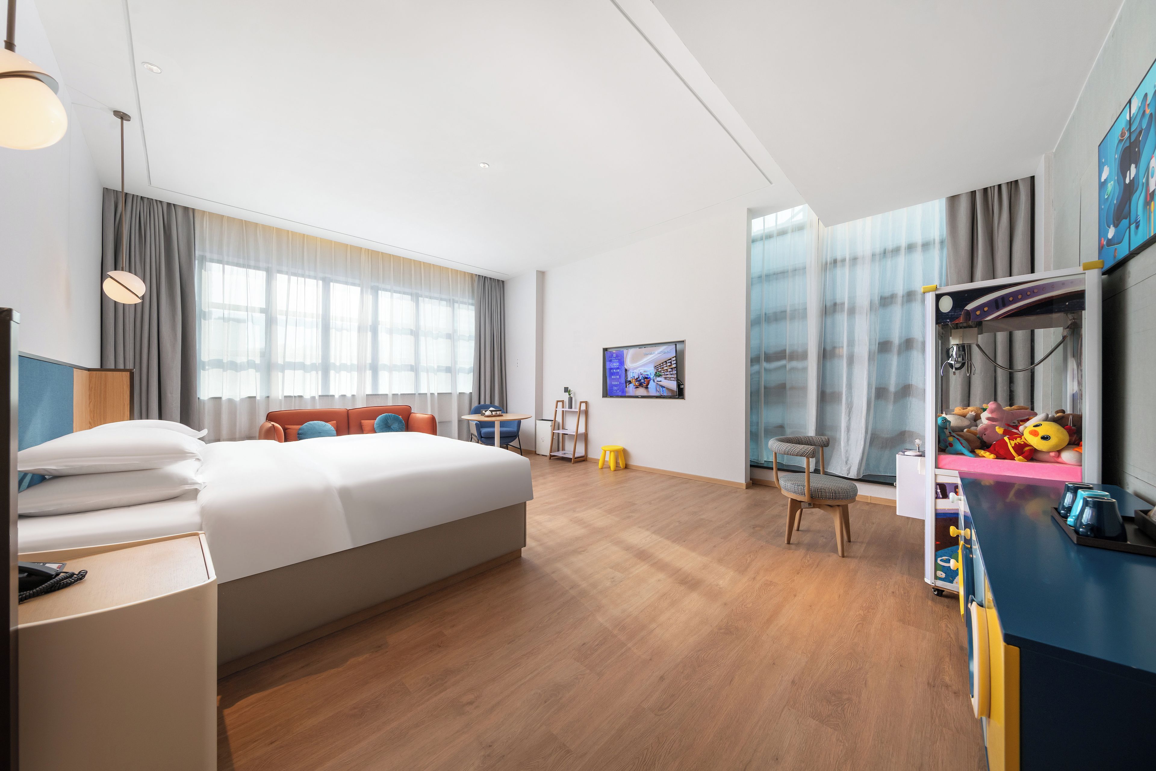 Habitació d'hotel moderna amb un llit gran, una taula de treball, una cadira, un televisor i una zona de jocs per a nens.