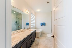 Un baño moderno con un espejo grande, dos lavamanos, una bañera y una ducha.