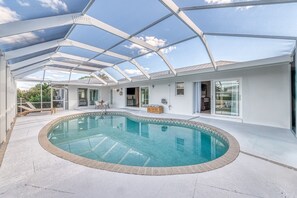 Un espace piscine couvert, doté d’une structure en verre, d’une chaise longue et d’une petite table.