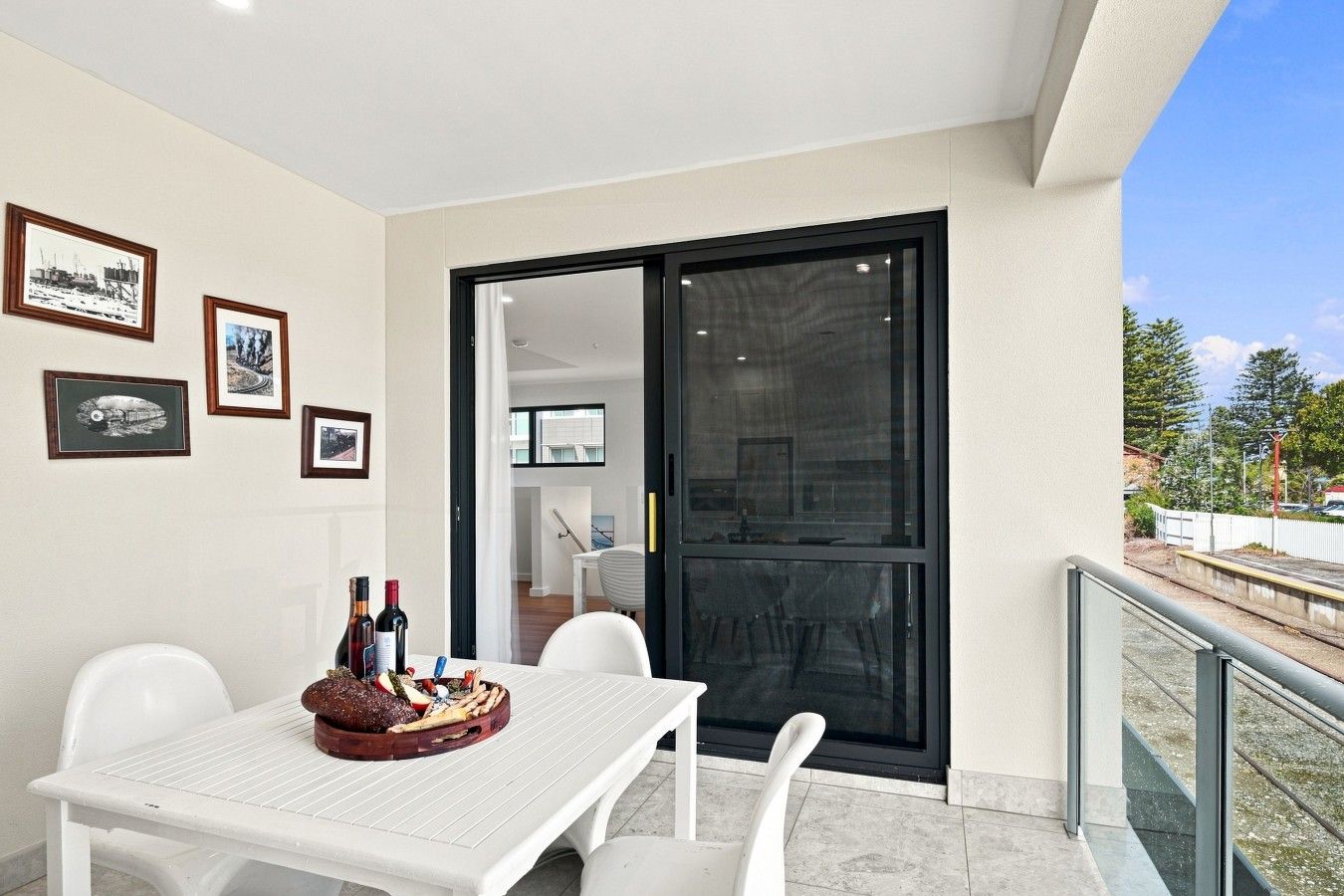 A balcony with a table set for dining, framed pictures on the wall, and a view of the outside.