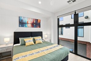 A modern hotel room with a large bed, a cityscape painting, and a view of the building's exterior through a glass door. - Modern 2BR Townhouse | Coastal Views, Double Garage & Steps to the Beach (Victor Harbor)