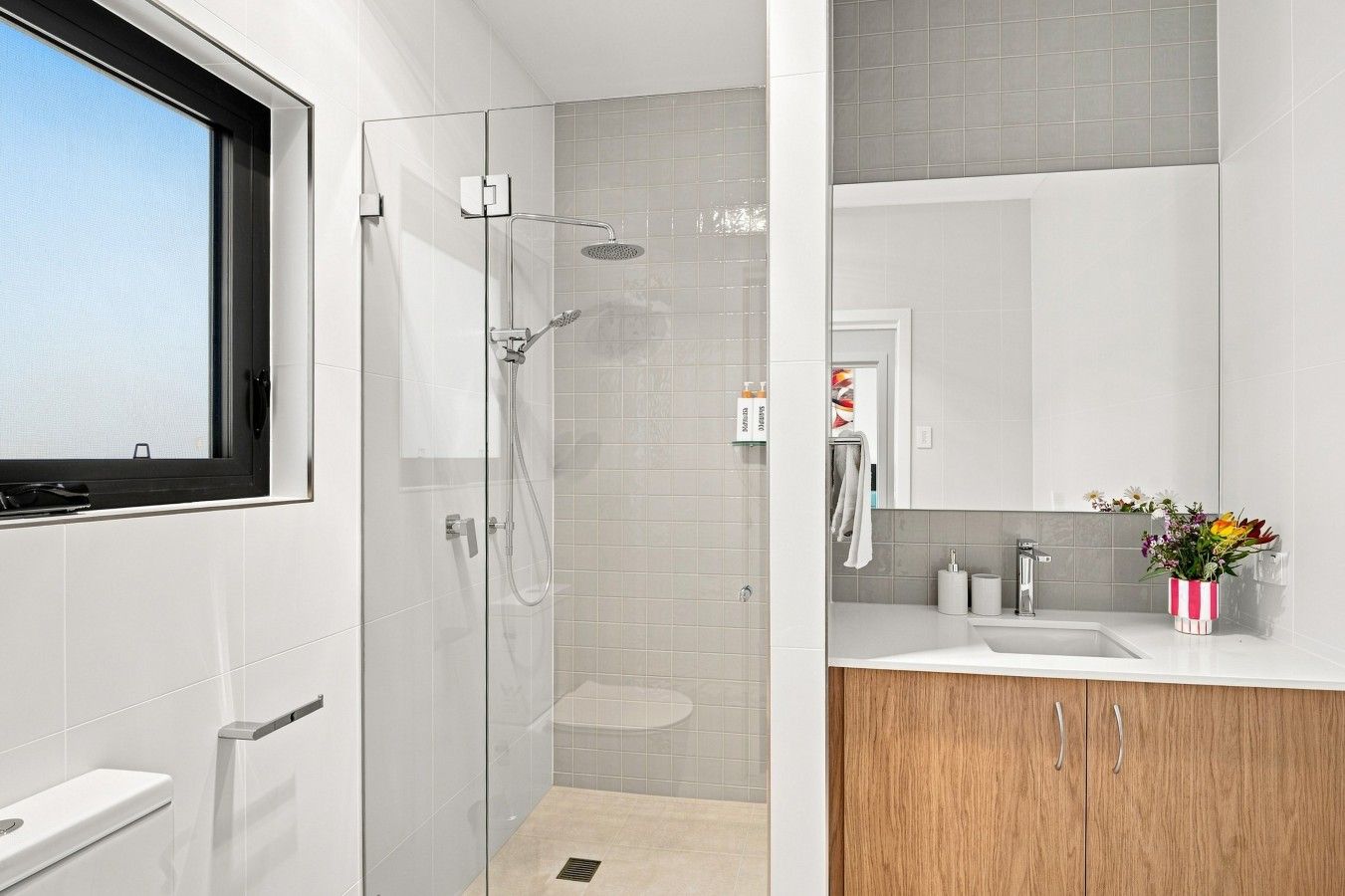 A modern bathroom with a glass-enclosed shower, a toilet, a sink with a mirror, and a wooden cabinet.