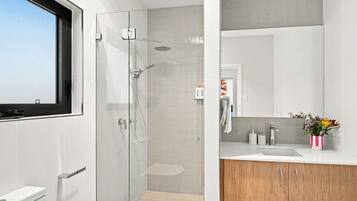 A modern bathroom with a glass-enclosed shower, a toilet, a sink with a mirror, and a wooden cabinet.