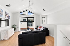 A spacious living area with a black sofa, a white cabinet, and a ceiling fan. - Modern 2BR Townhouse | Coastal Views, Double Garage & Steps to the Beach (Victor Harbor)