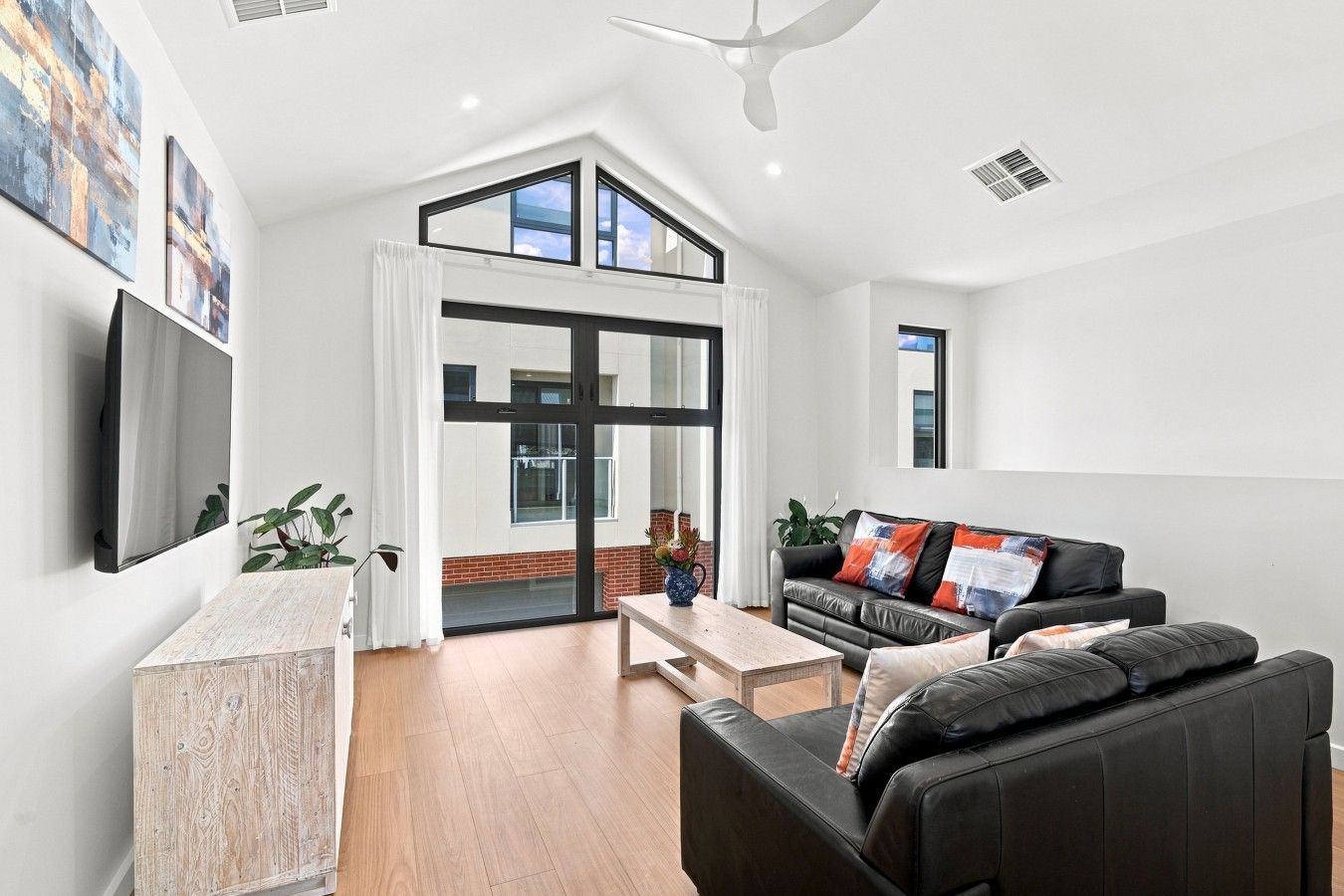 A modern living room with a black leather sofa, a wooden coffee table, and a flat-screen TV mounted on the wall.