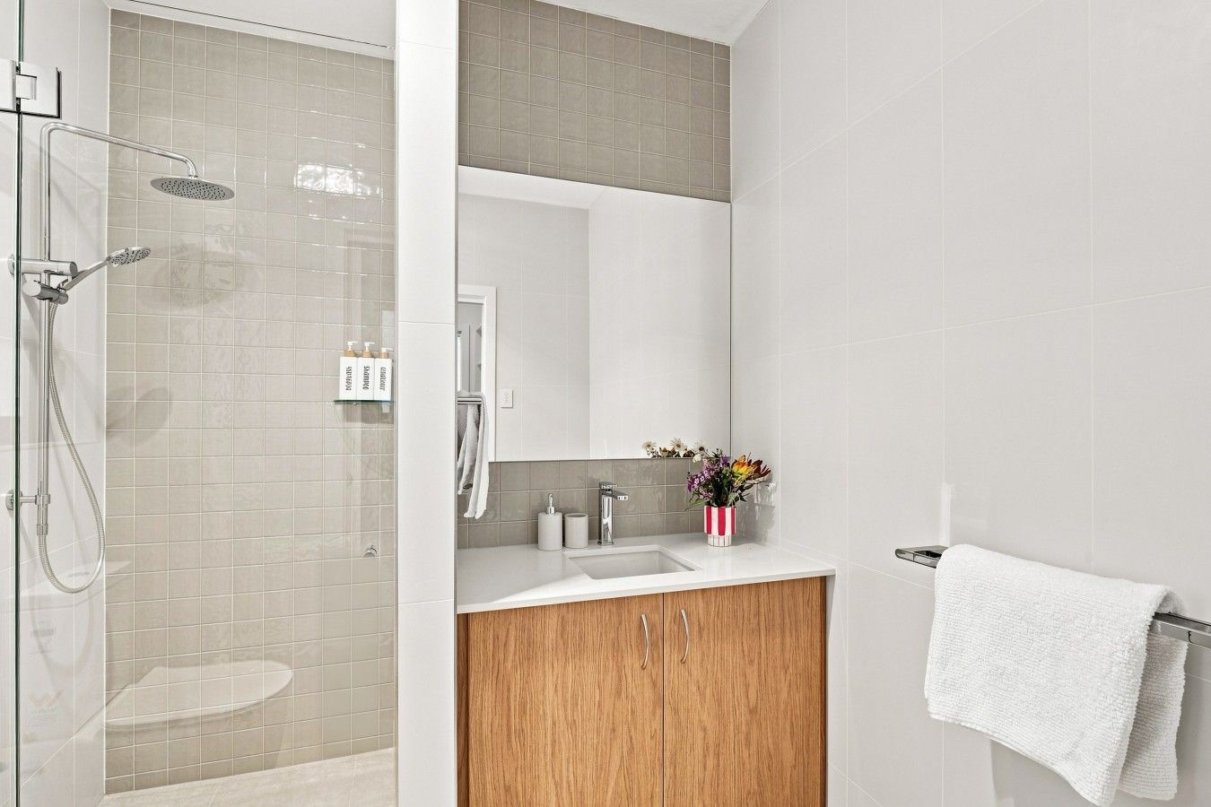 A modern bathroom with a glass shower enclosure, a wooden vanity, and a white sink.