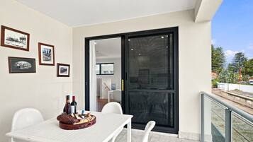 A balcony with a table set for dining, framed pictures on the wall, and a view of the outside.