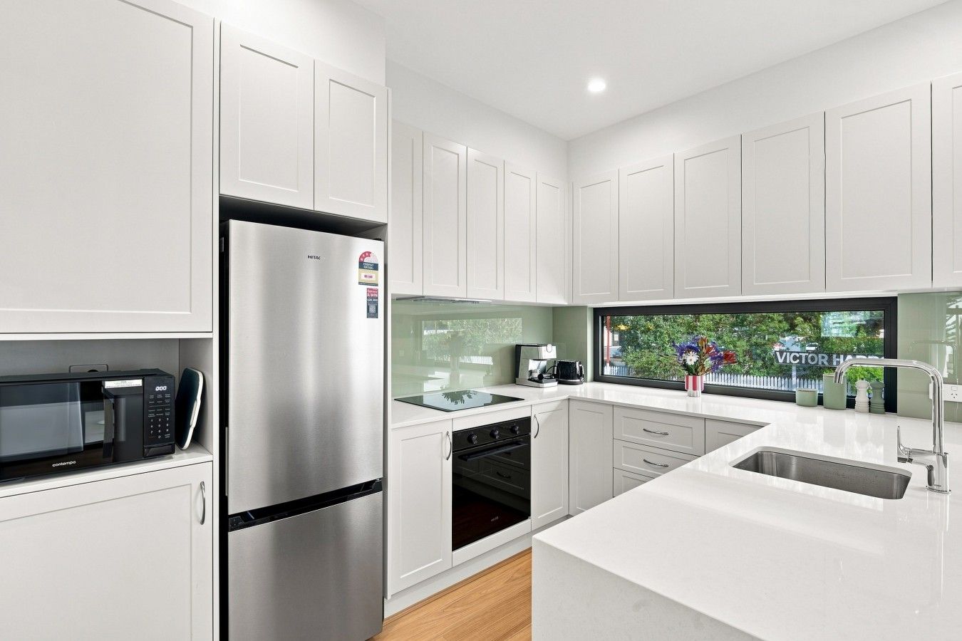 A modern kitchen with white cabinetry, stainless steel appliances, and a view of a garden through a window.