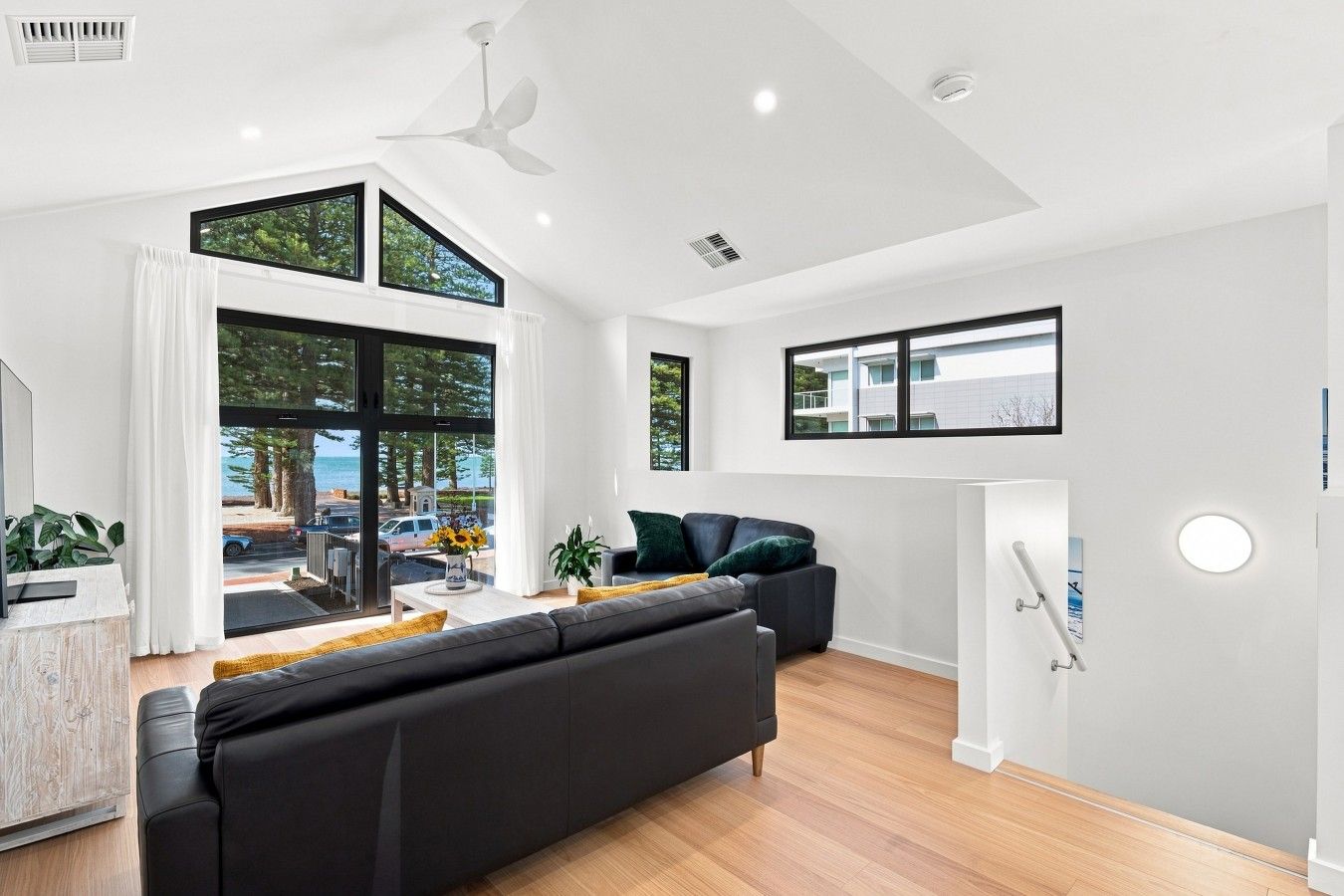 A modern living room with a black sofa, a coffee table, and a view of the sea through large windows.