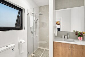 A modern bathroom with a glass shower enclosure, a toilet with a paper towel dispenser, and a vanity with a sink and a mirror.