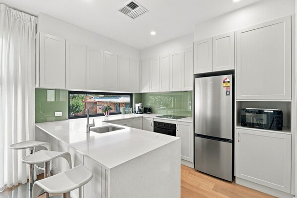 A modern kitchen with white cabinetry, a stainless steel refrigerator, a built-in oven, and a microwave.
