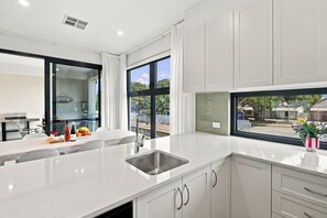 A modern kitchen with a large window, white cabinetry, and a countertop with a sink.