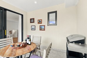 A dining area with a wooden table, chairs, a grill, and framed pictures on the wall. - Modern 2BR Townhouse | Coastal Views, Double Garage & Steps to the Beach (Victor Harbor)