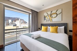 Ein Hotelzimmer mit einem großen Bett, Blick auf die Stadt und einem modernen abstrakten Gemälde an der Wand.