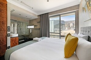 Ein Hotelzimmer mit einem großen Bett, einem Badezimmer mit Duschkabine und Blick auf die Stadt.
