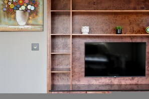A modern living room with a flat-screen TV mounted on a wooden wall, surrounded by shelves and a decorative painting. - Spacious Harbour Penthouse Two Bedroom Two Bathroom Harbour Mountain Views (Cape Town)