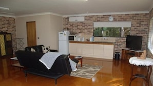 A living room with a black sofa, a small table, and a television on a stand. - Emerald Tropical Palms B&B (Coffs Harbour)