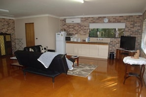 A living room with a black sofa, a small table, and a television on a stand. - Emerald Tropical Palms B&B (Coffs Harbour)