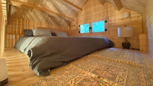 A wooden cabin bedroom with a bed, two windows, a nightstand, and a rug. - Forest Hideout - Peaceful Cabin Getaway in the woods (Duncan)