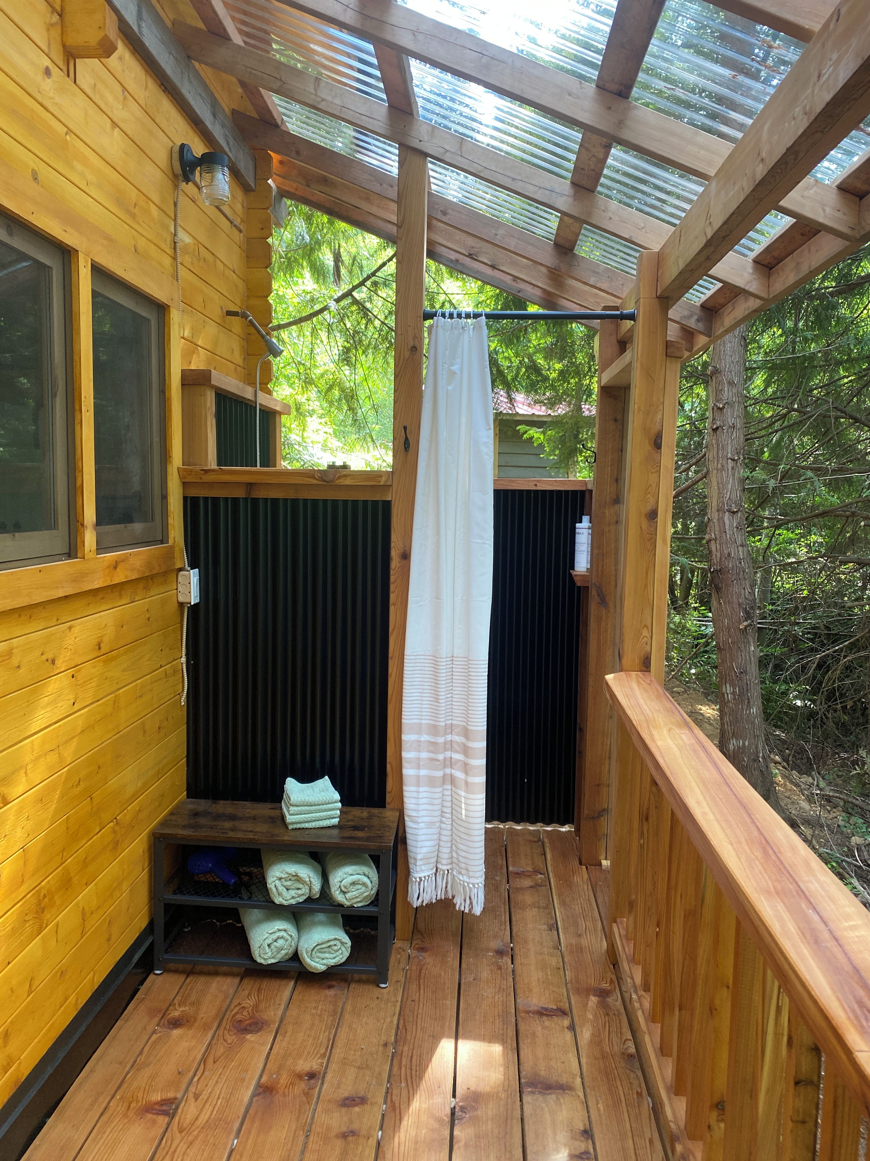 Una terraza de madera con zona de ducha, perchero y estante con toallas.