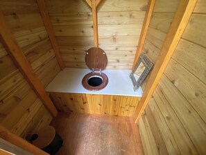 A small wooden cabin with a single wooden toilet and a mirror on the wall.