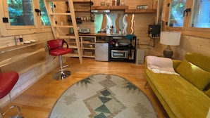 A compact cabin with a kitchenette, a dining area, and a living space with a sofa and a red chair. - Forest Hideout - Peaceful Cabin Getaway in the woods (Duncan)
