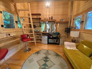A compact cabin with a kitchenette, a dining area, and a living space with a sofa and a red chair.