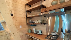 A compact kitchen with wooden walls, a built-in gas stove, and a small refrigerator. - Forest Hideout - Peaceful Cabin Getaway in the woods (Duncan)