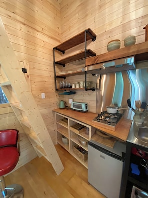A compact kitchen with wooden walls, a built-in gas stove, and a small refrigerator.
