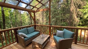 Een houten terras met rieten meubilair, waaronder een bank en stoelen, en een tafel.