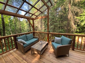 A wooden deck with wicker furniture, including a sofa and chairs, and a table.