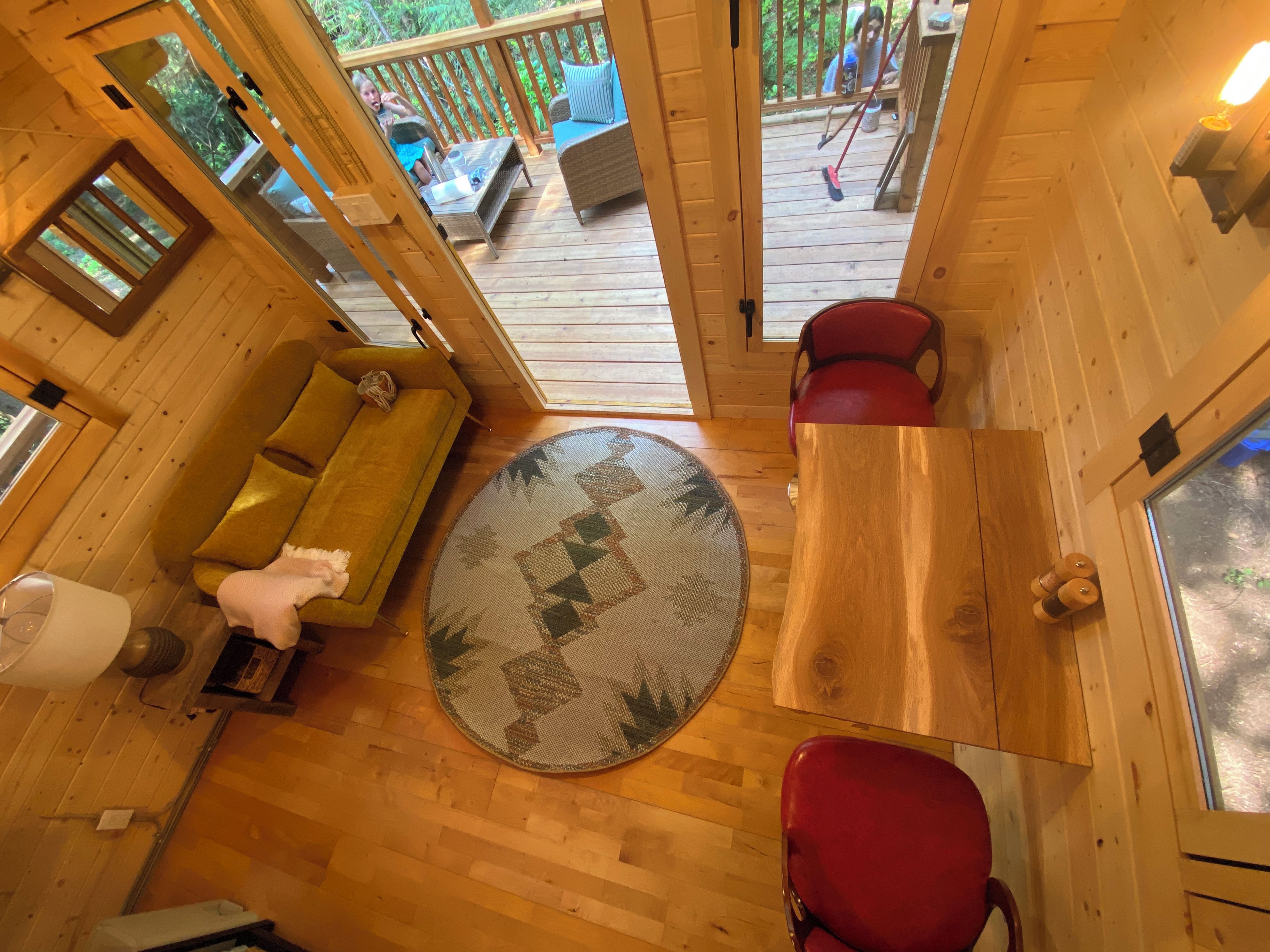 A wooden interior with a sofa, chairs, a round table, and a view of an outdoor deck.