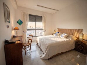 Ein Hotelzimmer mit Bett, Schreibtisch, Stuhl, Nachttisch mit Lampe und Blick auf die Stadt durch das Fenster.