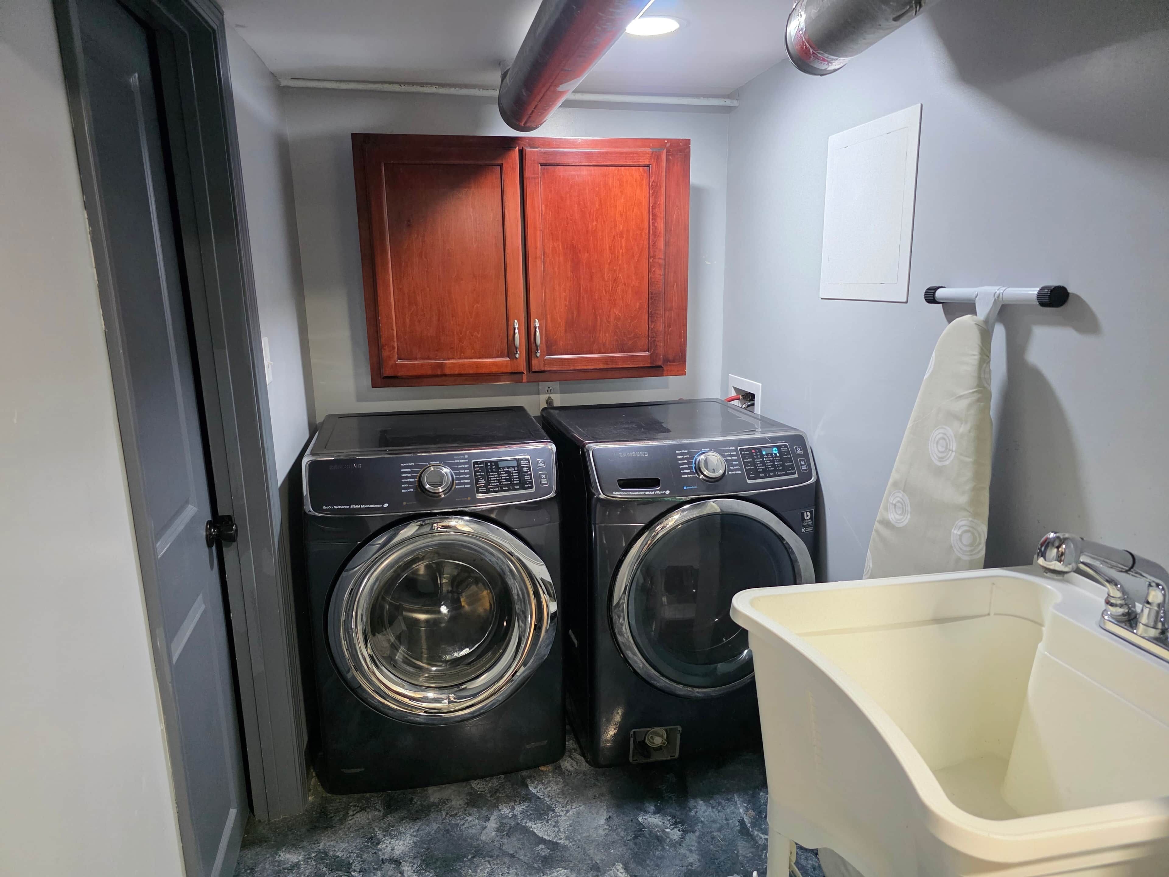 A laundry room with two washing machines, a sink, and wooden cabinets.