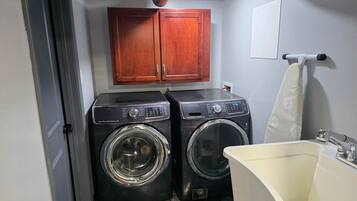 A laundry room with two washing machines, a sink, and wooden cabinets.
