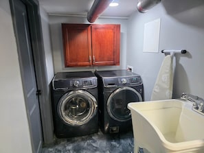 A laundry room with two washing machines, a sink, and wooden cabinets.