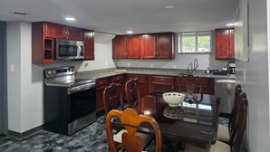 A kitchen with dark wooden cabinets, a stainless steel refrigerator, a microwave, and a stove. There is a dining table with chairs and a window above the sink. - The Hideaway | Cozy 2BR Retreat in Pontiac (Pontiac)