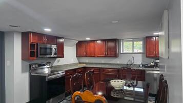 A kitchen with dark wooden cabinets, a stainless steel refrigerator, a microwave, and a stove. There is a dining table with chairs and a window above the sink.