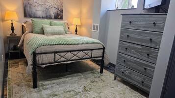 A bedroom with a bed, two bedside lamps, a dresser, and a large window.