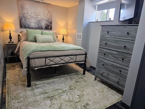A bedroom with a bed, two bedside lamps, a dresser, and a large window.
